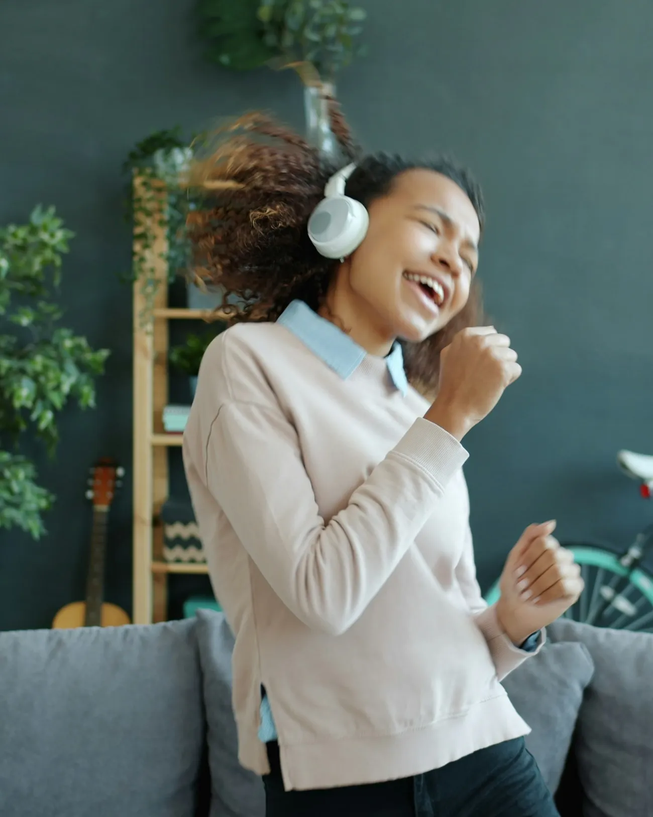 A woman in headphones singing along and dancing at home